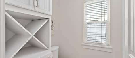 A bathroom with a toilet, a white cabinet, and a window with blinds.