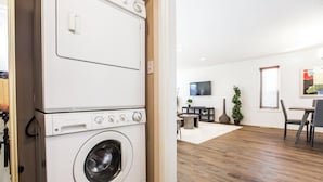 A laundry room with stacked washers and dryers, a dining area with a table and chairs, and a living room with a TV and decorative items. - Chic 3BR Modern Home - Wi-Fi - Netflix - Sleeps 8! (Edmonton)