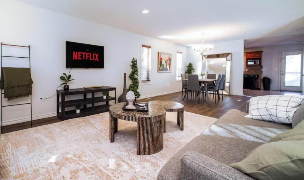 A modern living room with a flat-screen TV, a dining area, and a kitchen in the background.