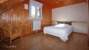 Ein Zimmer mit Holzwänden, einem Bett, einem Sessel und einem Fenster.