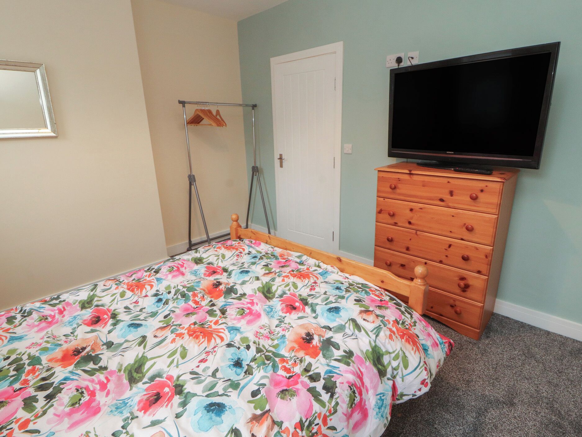 Un dormitorio con edredón estampado con flores, un aparador de madera, un televisor y una puerta.