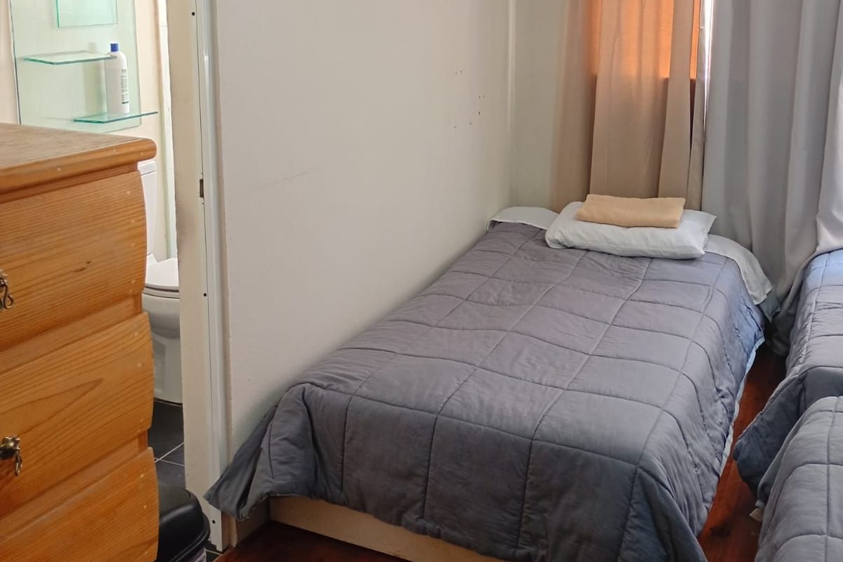 A bedroom with a single bed, a wooden dresser, and a glass cabinet.