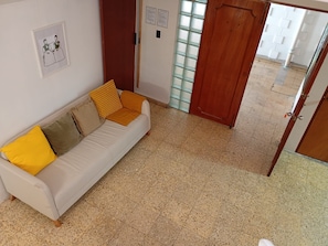 A room with a white sofa, a wooden door, and a tiled floor. - Hostal Kahlo (Ciudad de México)