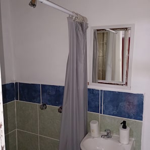 A bathroom with a shower curtain, a window, a sink with a soap dispenser, and a towel rack. - Hostal Kahlo (Ciudad de México)