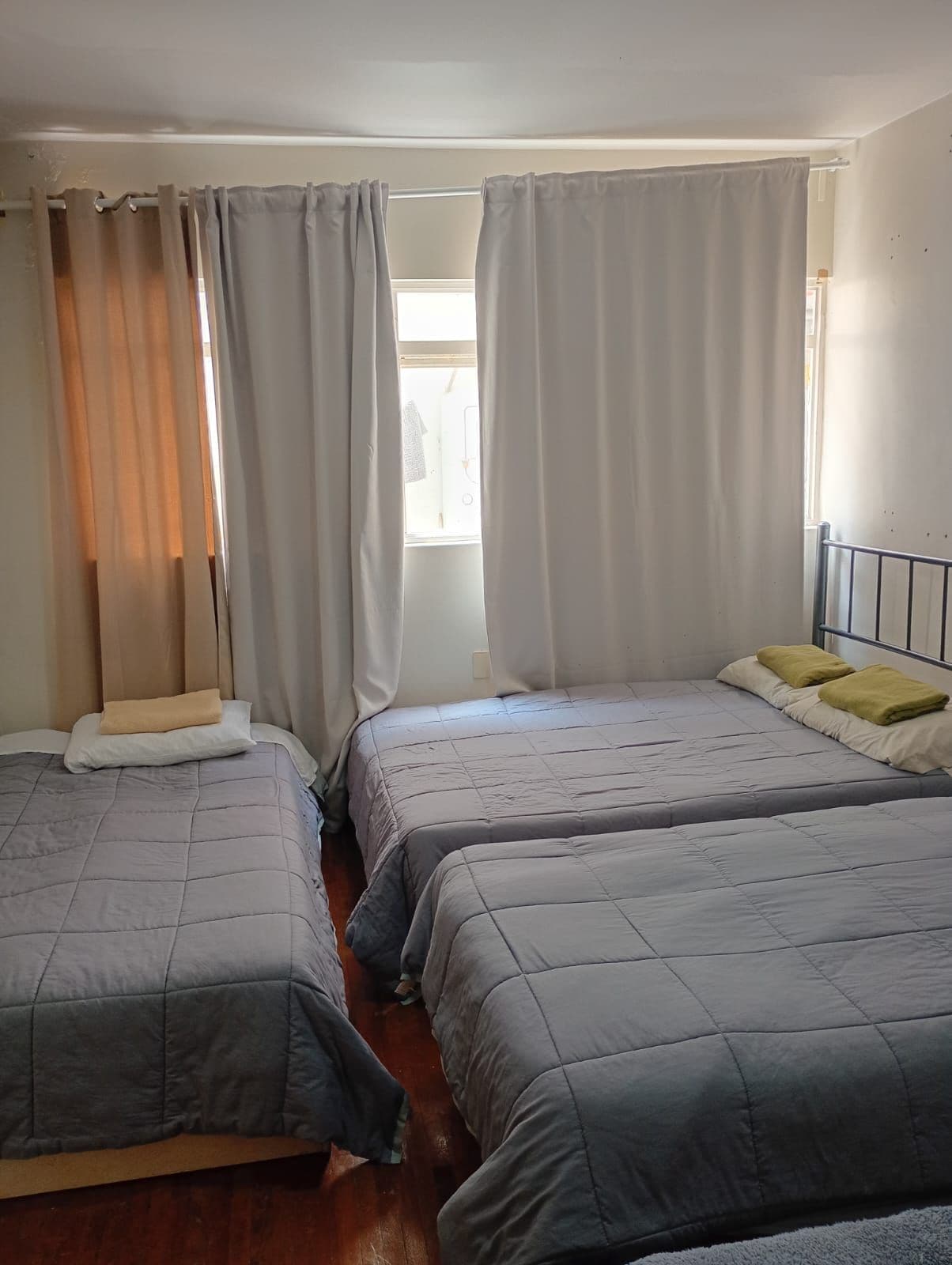 Una habitación con dos camas, cada una con un edredón y almohadas grises, y un ventanal con cortinas.