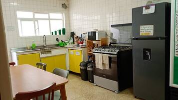 Una cocina con estufa, microondas y refrigerador. Hay una ventana sobre el fregadero y un cubo de basura cerca de la estufa.