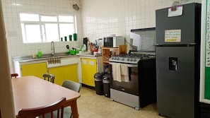 A kitchen with a stove, microwave, and refrigerator. There is a window above the sink and a trash can near the stove. - Hostal Kahlo (Ciudad de México)