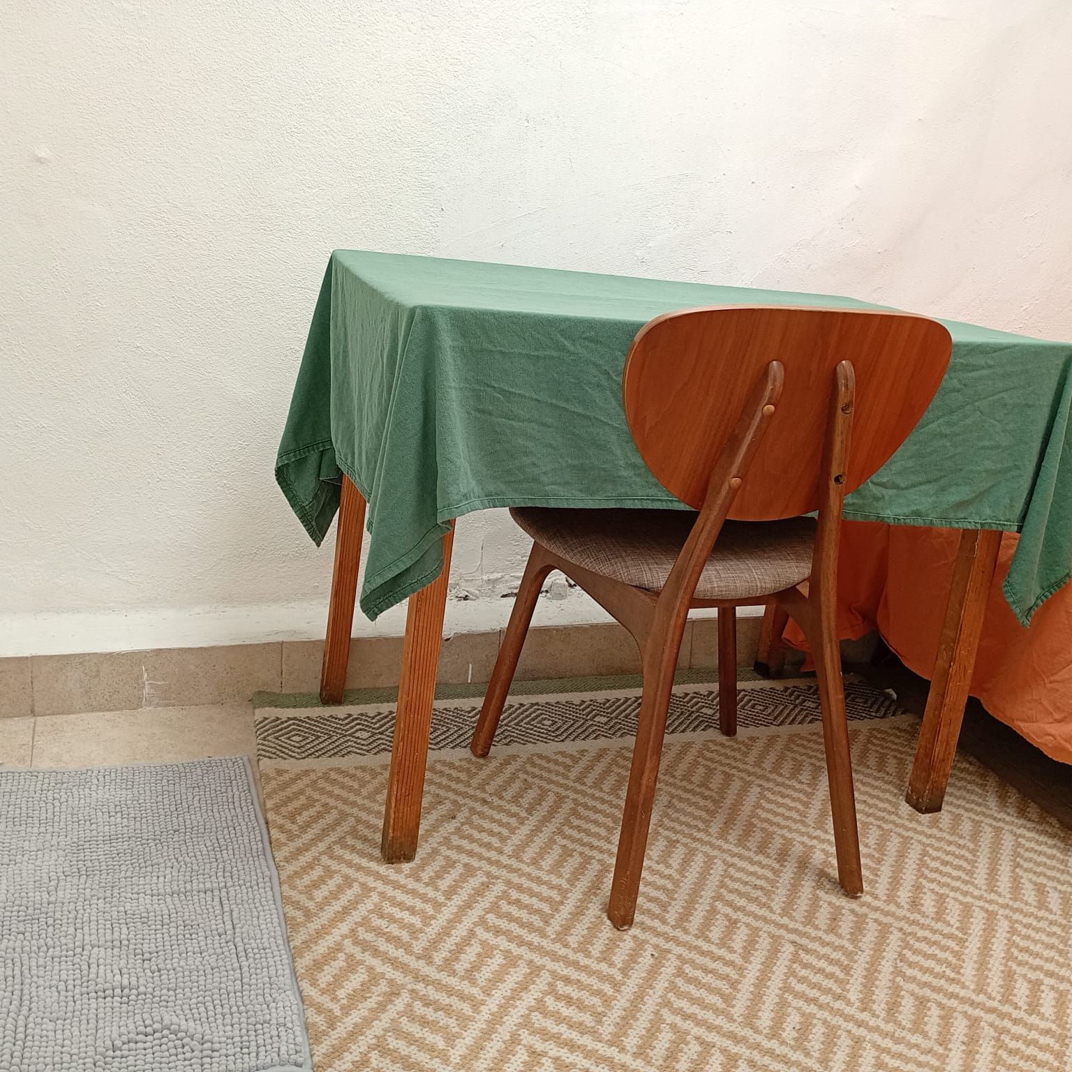 Un comedor con una mesa cubierta por un mantel verde, una silla de madera y una alfombra estampada.