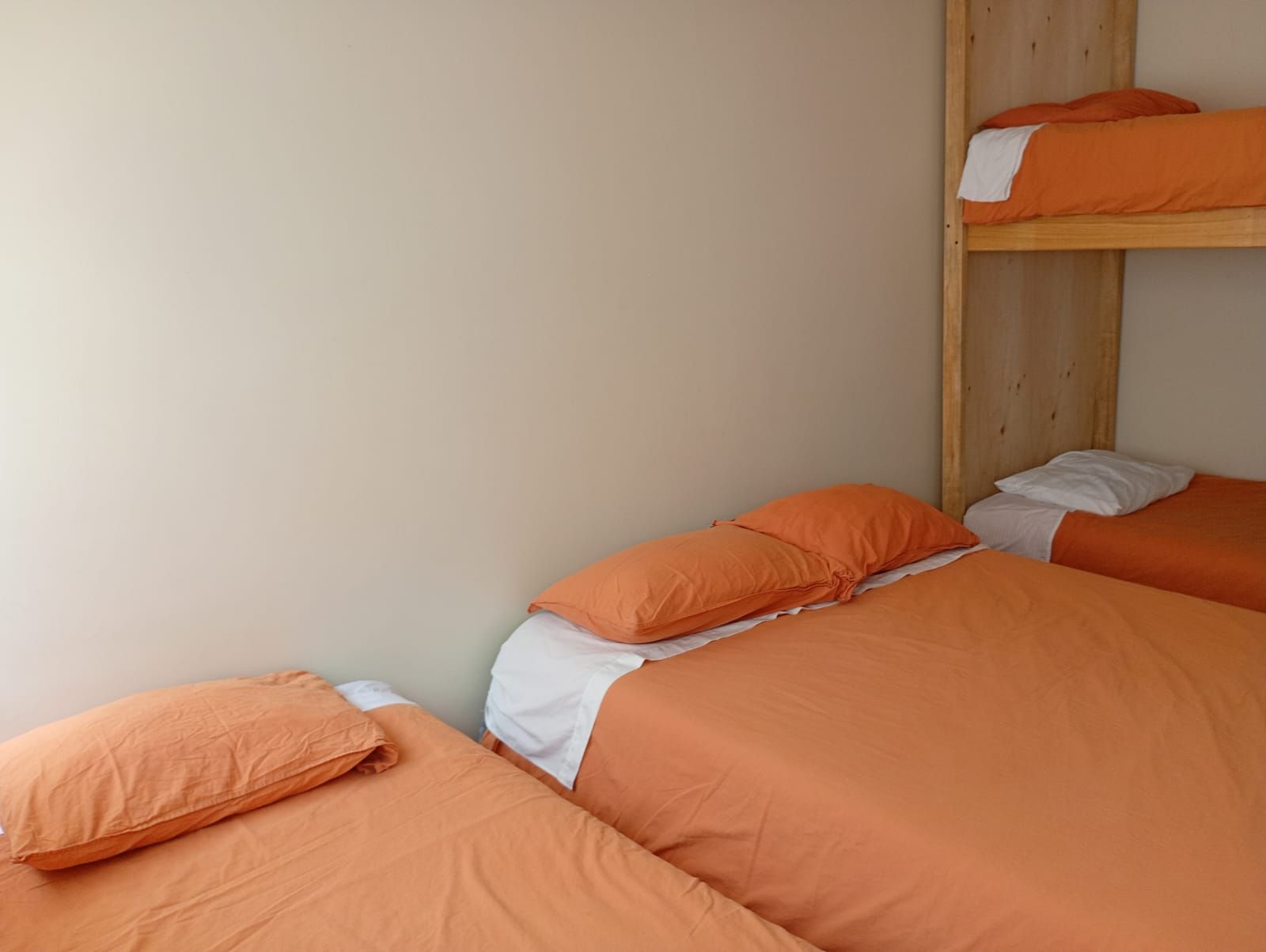 Quarto com duas camas de solteiro e uma cama beliche, tudo com roupa de cama laranja.