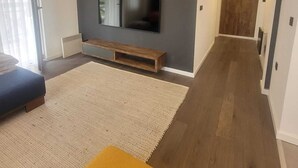 A modern living room with a flat-screen TV, a wooden bench, and a yellow ottoman. - Soothing 1-bedroom apartment in awesome Kopaonik getaway (Kopaonik)