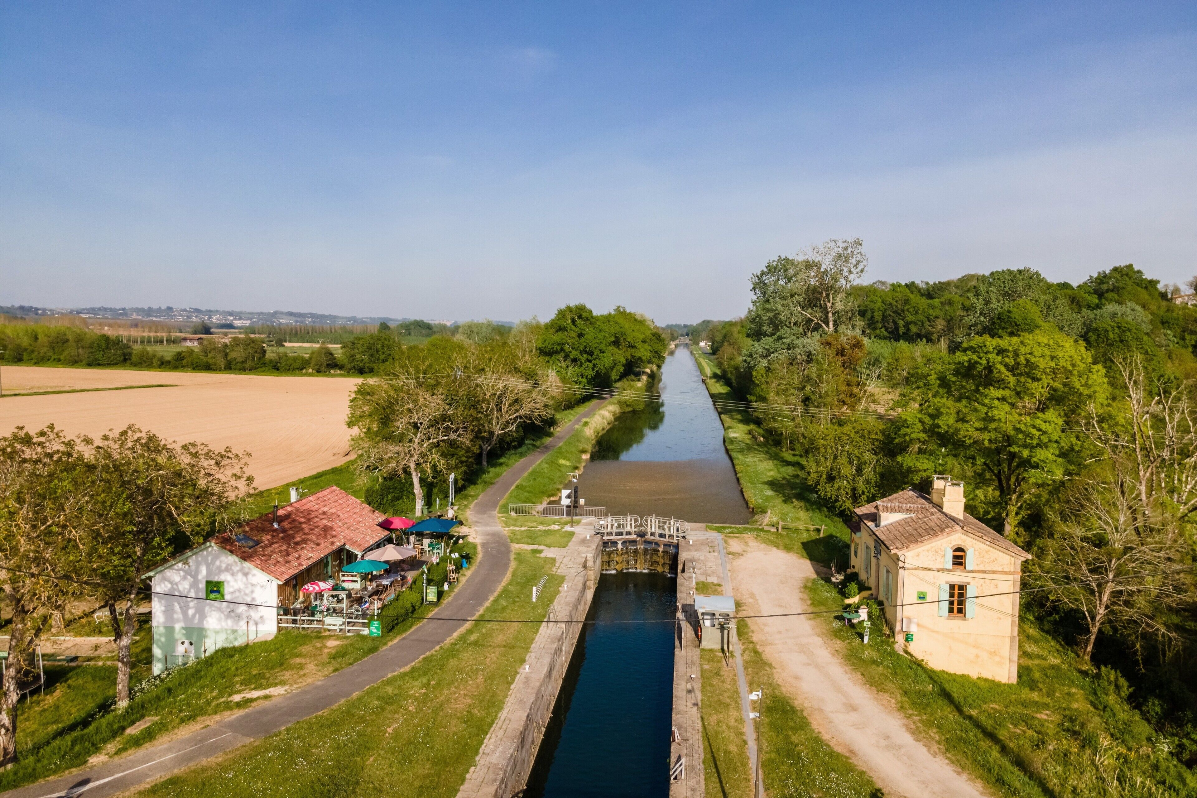 Un canal avec une écluse, bordé de verdure et surmonté d’un petit bâtiment doté d’un toit rouge.