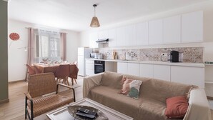 Eine moderne Küche mit weißen Schränken, ein Essbereich mit Tisch und Stühlen sowie eine Wohnbereich mit einer Couch und einem Couchtisch.