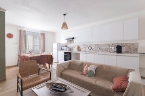A modern kitchen with white cabinets, a dining area with a table and chairs, and a living area with a sofa and a coffee table. - Le Carmen apartment in the heart of Saint-Hippolyte, 3 bedrooms, up to 6 guests (Saint-Hippolyte)