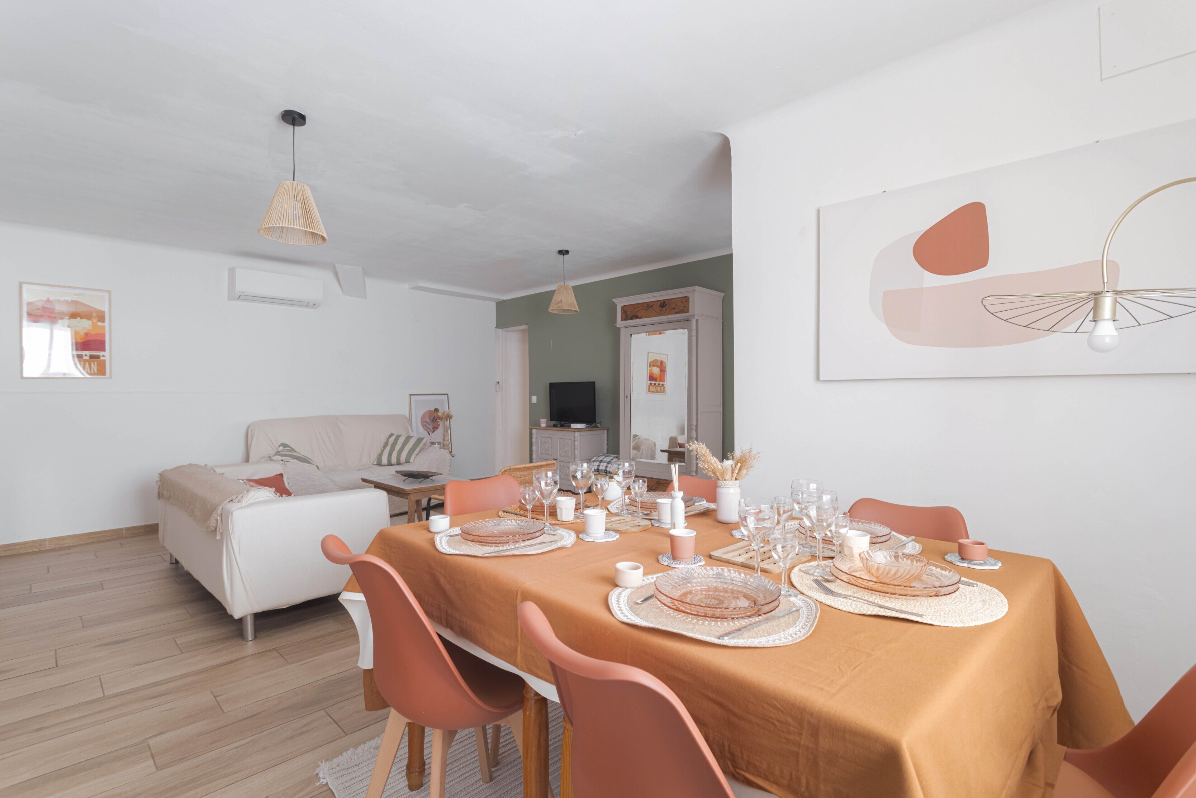 A dining room with a table set for six, chairs, a sofa, and a television in the background.