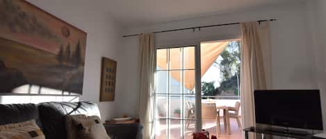 Uma sala de estar com um sofá de couro, uma mesa de centro de vidro com livros e flores, uma TV de tela plana e uma pintura grande na parede.