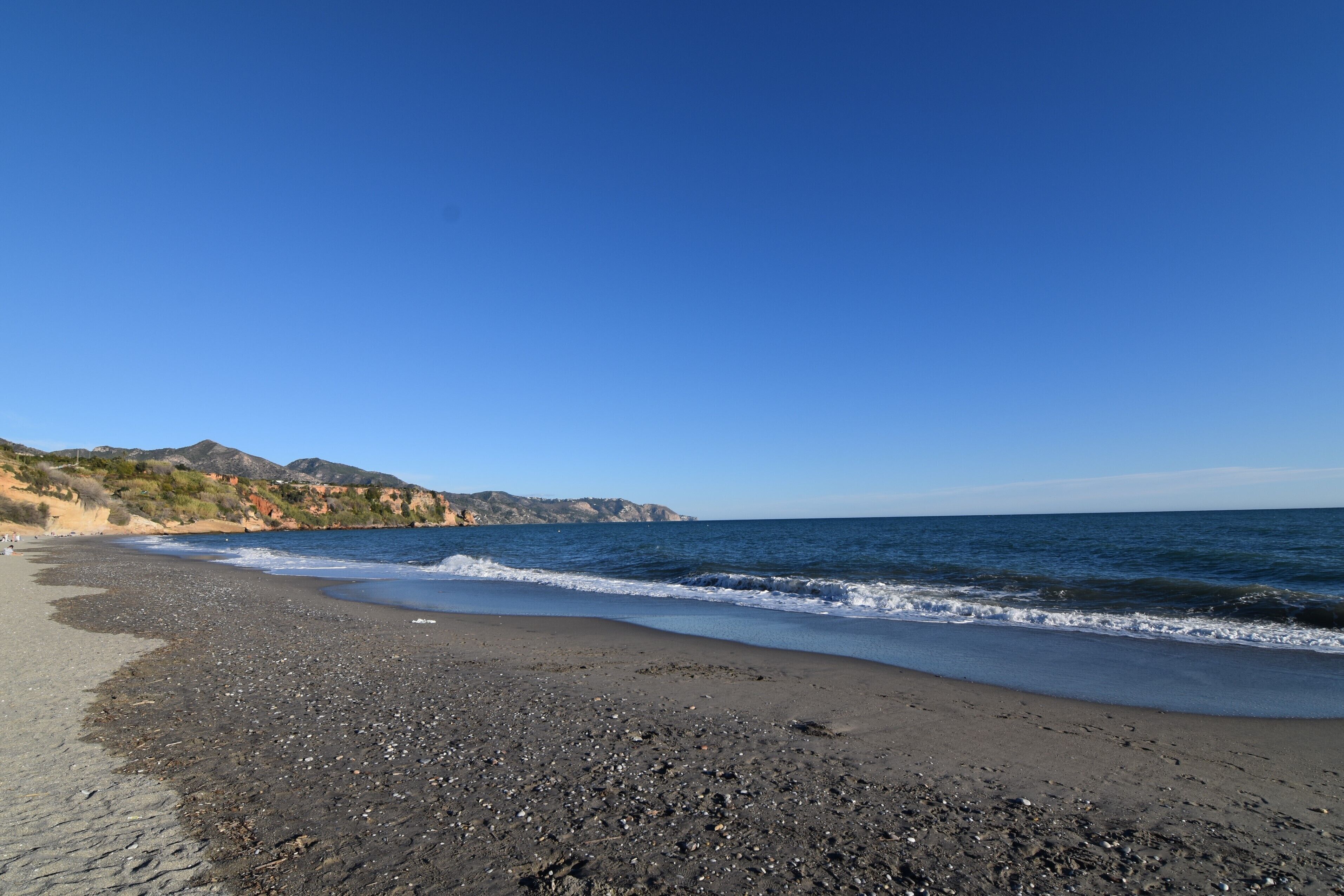 Une plage bordée d’une côte rocheuse, sous un ciel bleu et dégagé.