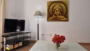 A living room with a flat-screen TV, a lamp, a Buddha painting, and a vase with flowers on a table. - Corinto Apartment, 100m from Burriana Beach (Nerja)