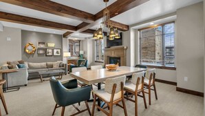 A spacious living room with a large wooden dining table, blue chairs, and a fireplace. - Sunrise Gondola Lodge - Ski-in/ski-out (Park City)