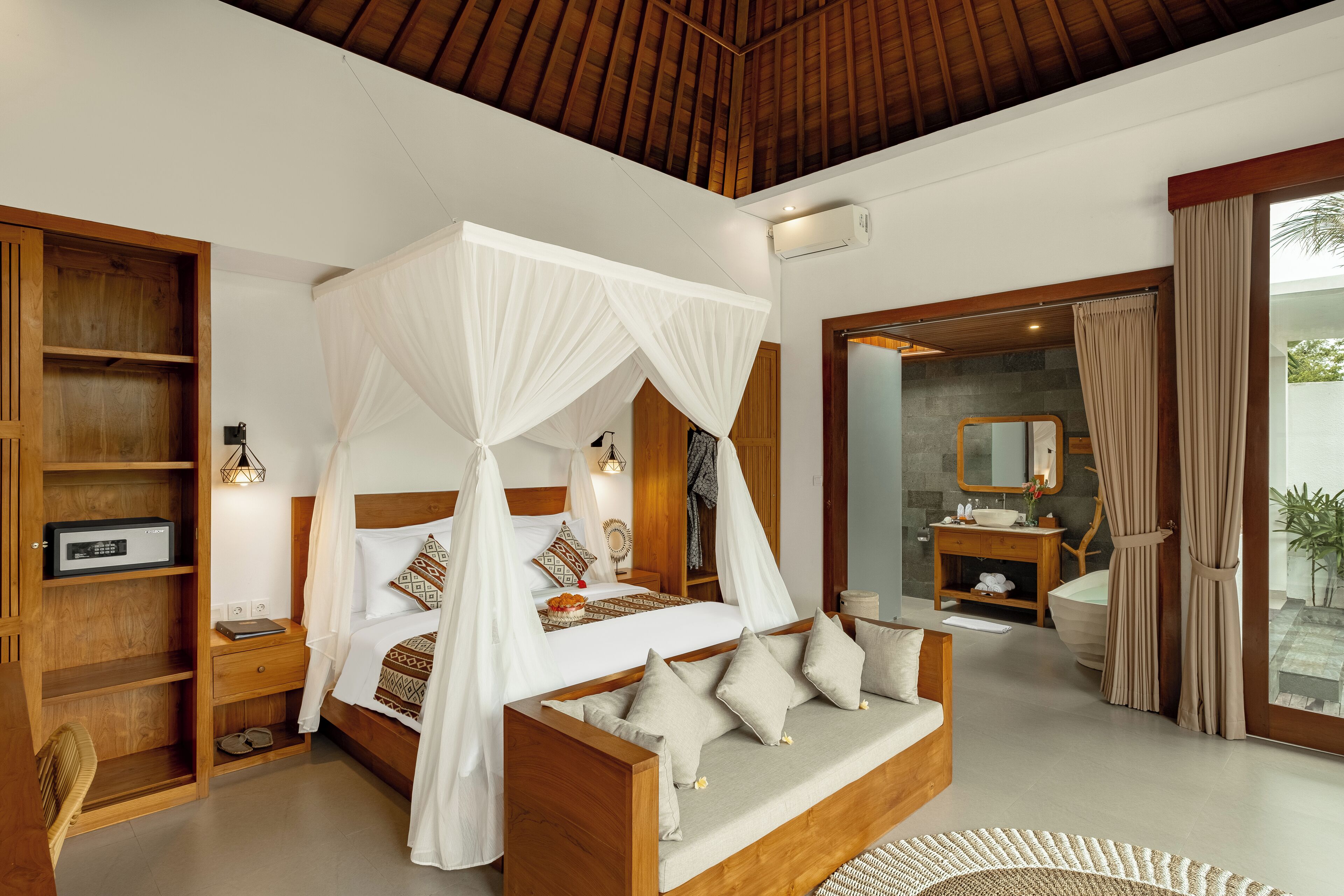 A bedroom with a canopy bed, wooden furniture, a bedside table with a radio, and a bathroom with a vanity and mirror.
