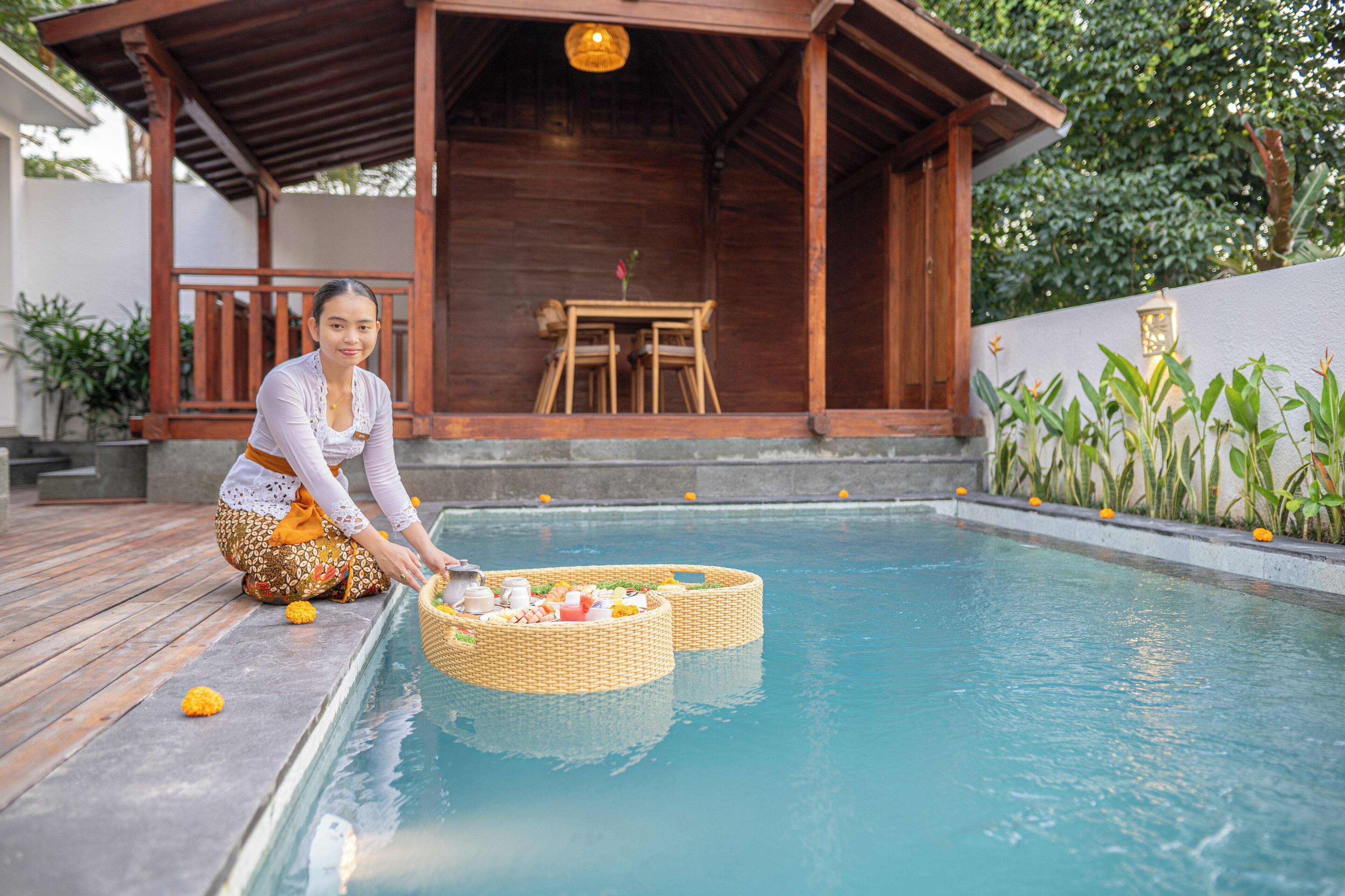 A poolside area with a wooden deck, a covered seating area, and a table with chairs.
