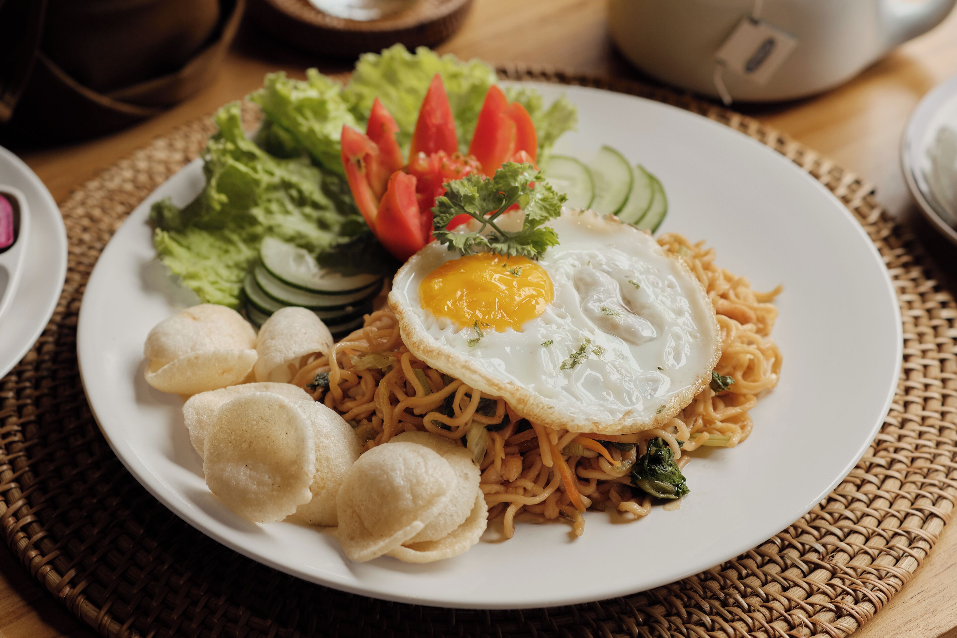 A plate of noodles with a fried egg, vegetables, and bread rolls.