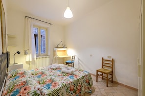 Un dormitorio con cama, escritorio con silla, lámpara y ventana con cortinas.