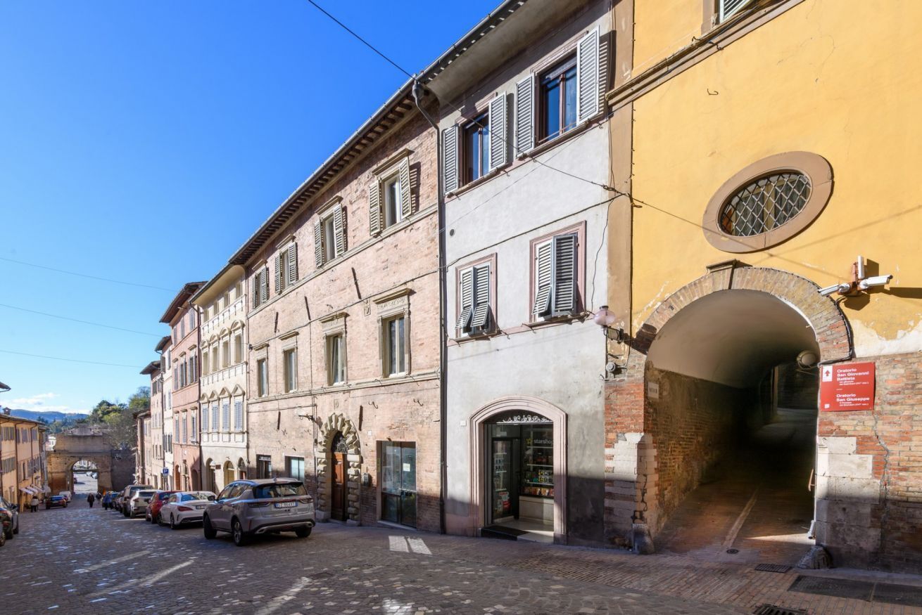 A street with historic buildings, a cobblestone road, and parked cars.