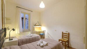 Ein Schlafzimmer mit zwei Betten, einem Schreibtisch, einem Stuhl, einer Lampe und einem Fenster.