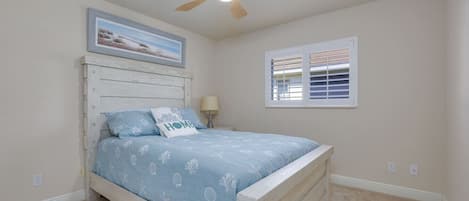 A bedroom with a bed, a ceiling fan, a window with blinds, and a wall-mounted picture.