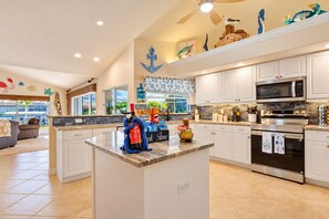 A spacious kitchen with white cabinetry, a central island, and a view to the outside. - Gulf Access•Glass-Bottom Tiki•FREE Heated Pool•Smart TVs•Kayaks•Beach/Fish Gear (Cape Coral)