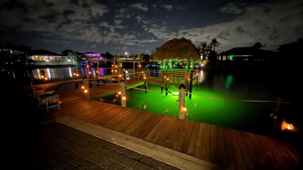 Une terrasse en bois avec une piscine, une structure à toit de chaume et un éclairage d’ambiance.