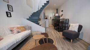 A modern living room with a sofa, two chairs, a coffee table, and a staircase leading to an upper level. - Romy's House (Thuir)