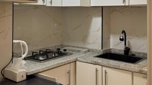A compact kitchen with white cabinets, a built-in microwave, a gas stove, and a washing machine. - Abdali elite studio (Amman)