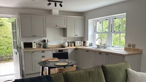 Une cuisine moderne avec des meubles blancs, une table à manger et un canapé vert agrémenté de coussins à motifs.