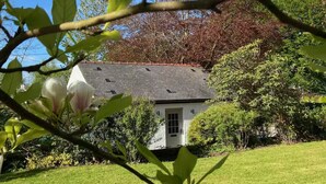 Une maison blanche avec un toit sombre, entourée d’herbe verte et d’arbres.