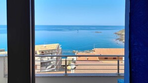 Uitzicht op de kust vanaf een balkon, met een heldere lucht, een rustige zee en gebouwen met pannendaken.