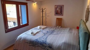 Een slaapkamer met een bed, een raam, een kapstok, een stoel en een schilderij aan de muur.