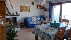 Een woonkamer met een blauwe bank, een wereldkaart aan de muur, een gitaar en een tafel met een tafelkleed met dessin.
