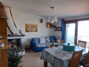 Un salon avec un canapé bleu, une carte du monde accrochée au mur, une guitare et un coin repas comprenant une table et des chaises.