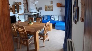 Een eetruimte met een houten tafel en stoelen, een blauwe bank en een keuken op de achtergrond.