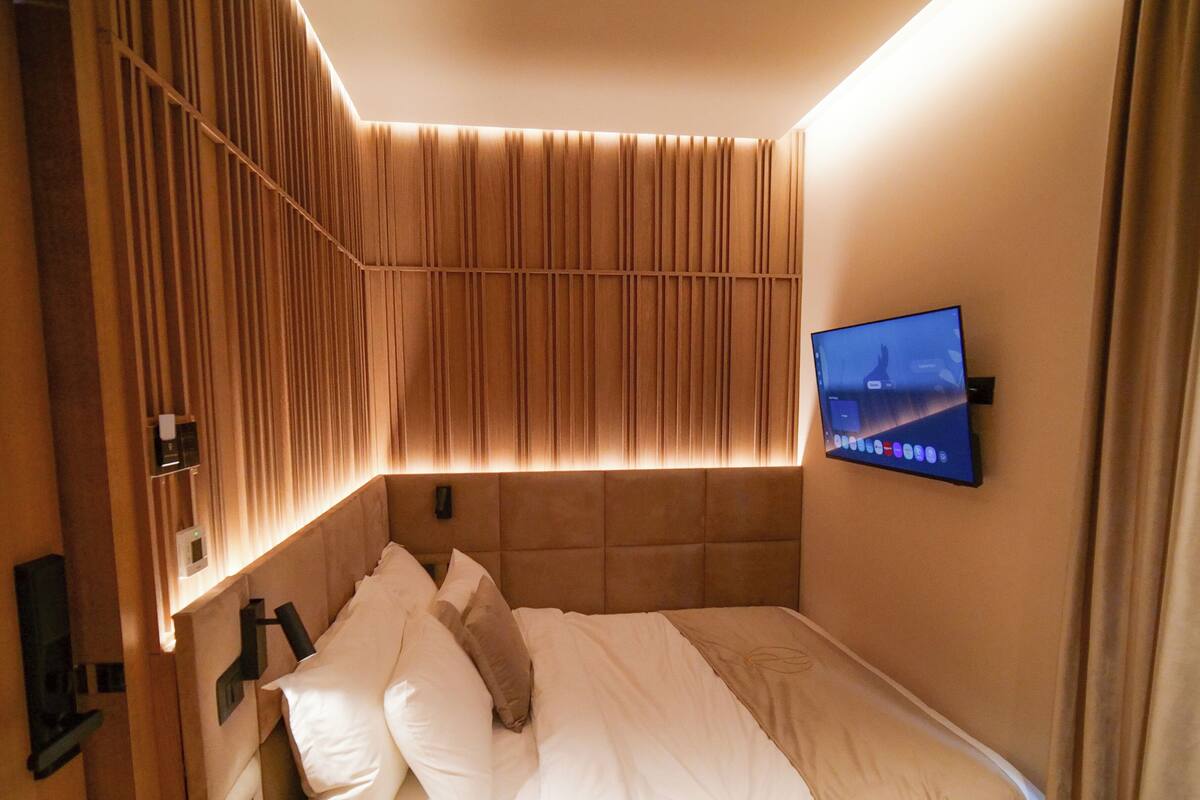 A hotel room with a bed, a mounted TV, and a wall with vertical slats.
