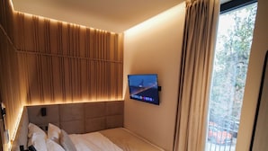 A modern bedroom with a bed, a mounted TV, and a view of the outside. - Post Inn  (Tirana)