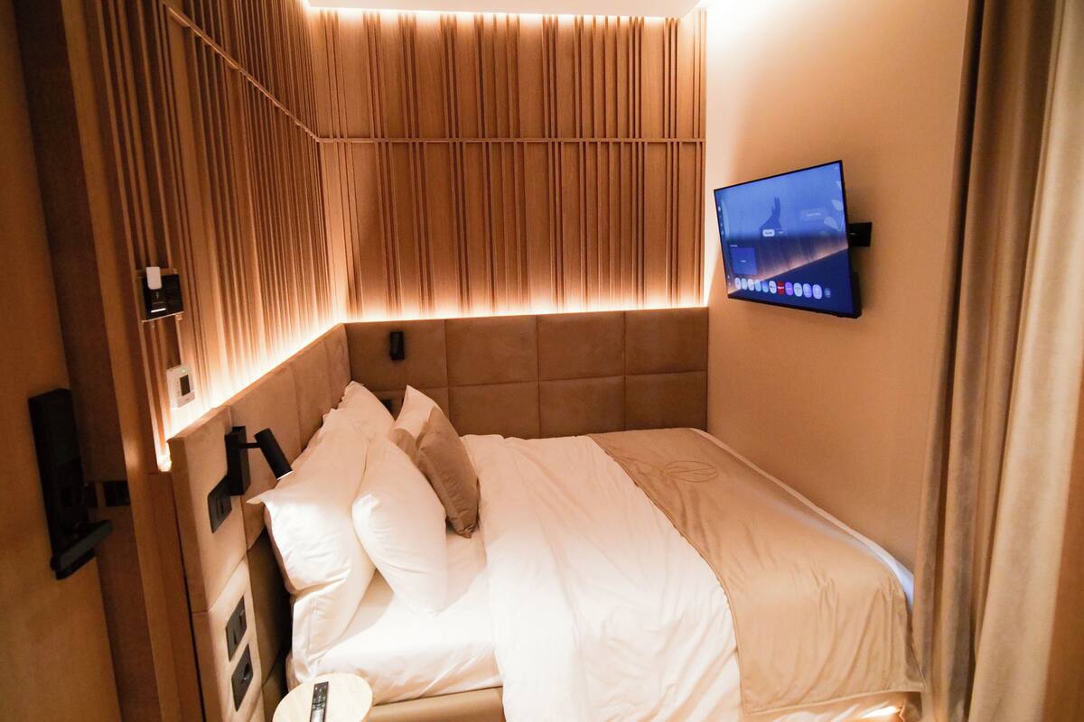 A hotel room with a bed, a flat-screen TV mounted on the wall, and a wall panel with vertical lines.