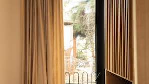 A window with curtains partially drawn, revealing a metal fence and greenery outside. - Post Inn  (Tirana)