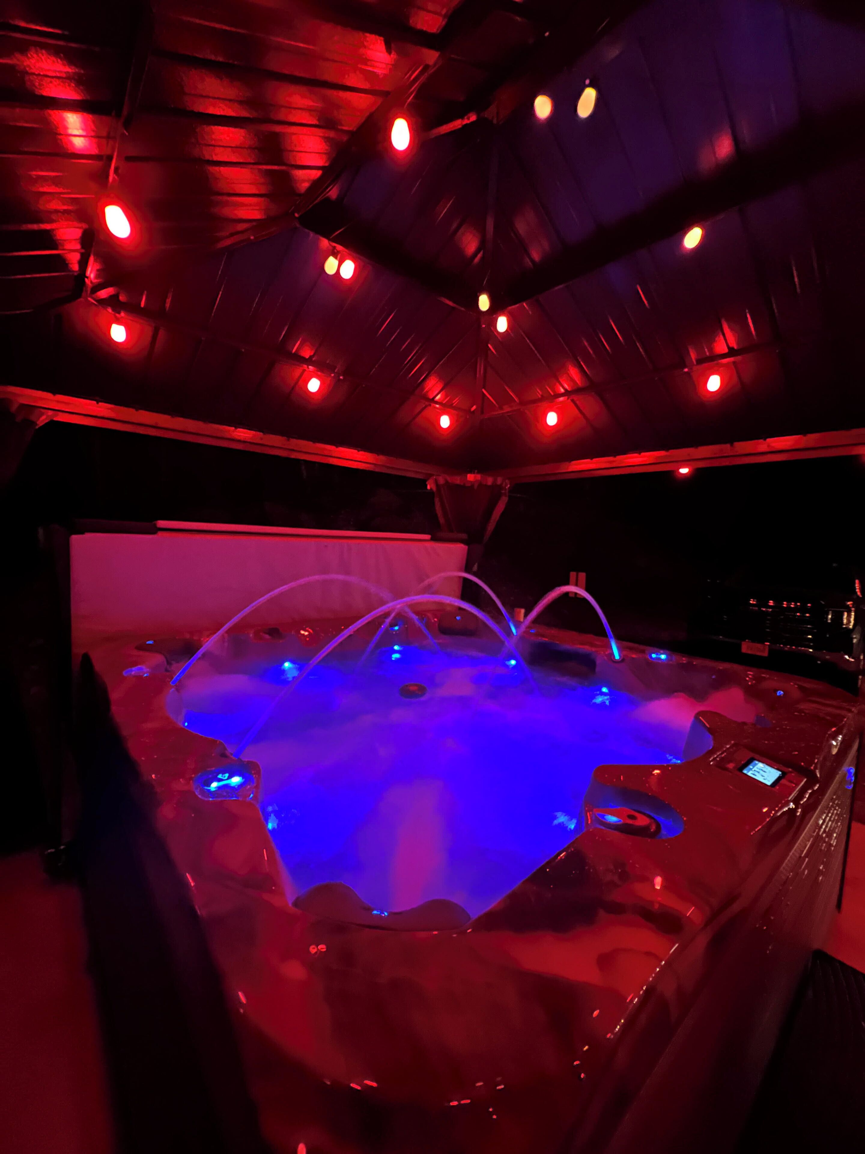 Un hidromasaje con iluminación azul y múltiples chorros, en un entorno oscuro con luces rojas.