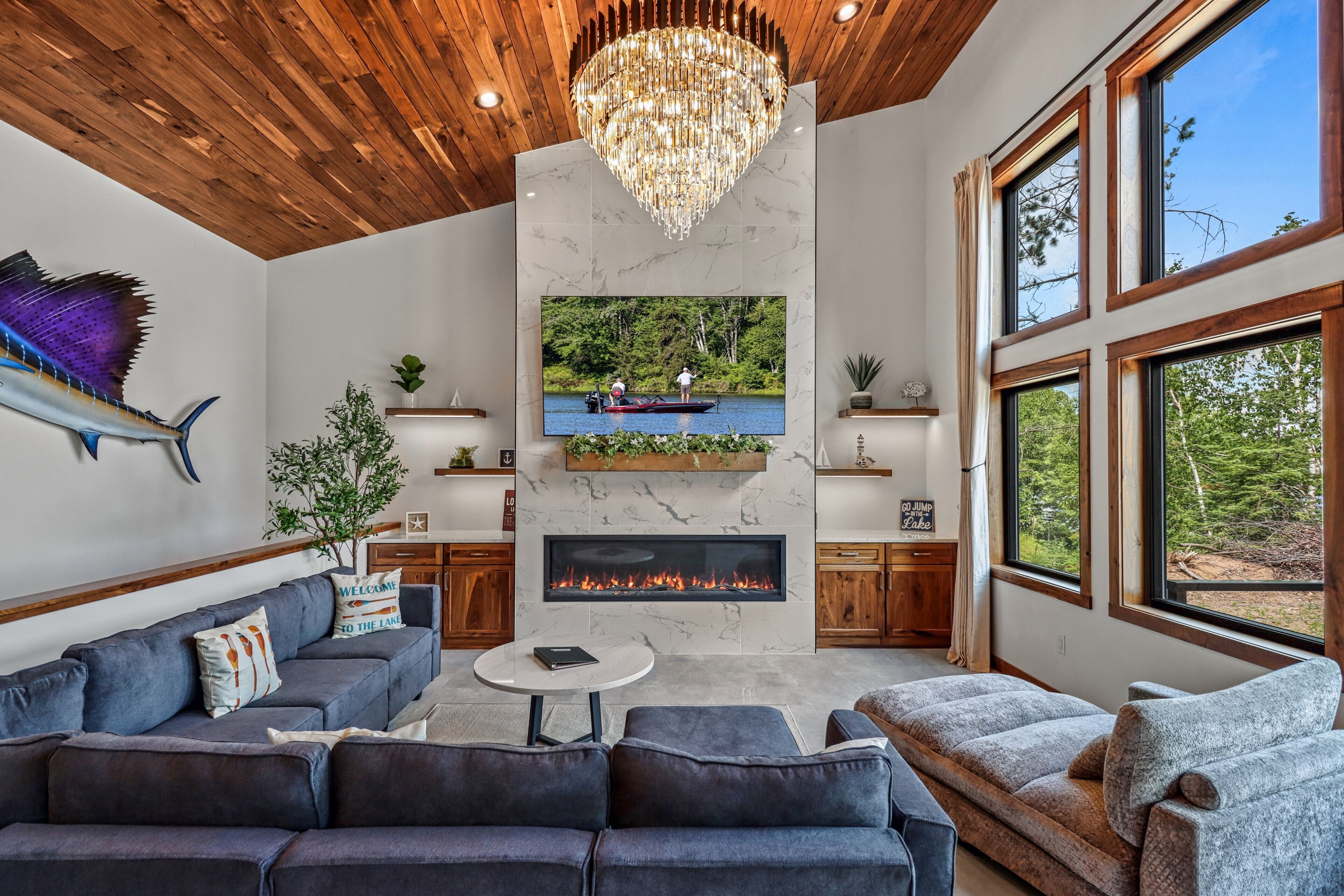 Una sala de estar moderna con chimenea, televisor montado y un ventanal grande con vistas a un bosque.