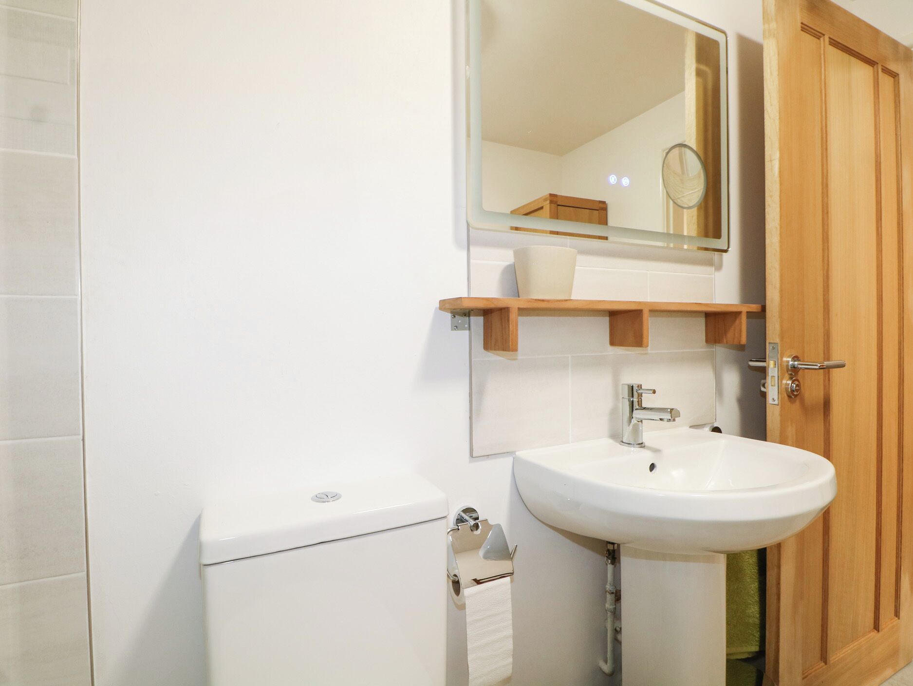 A bathroom with a toilet, sink, mirror, and wooden door.