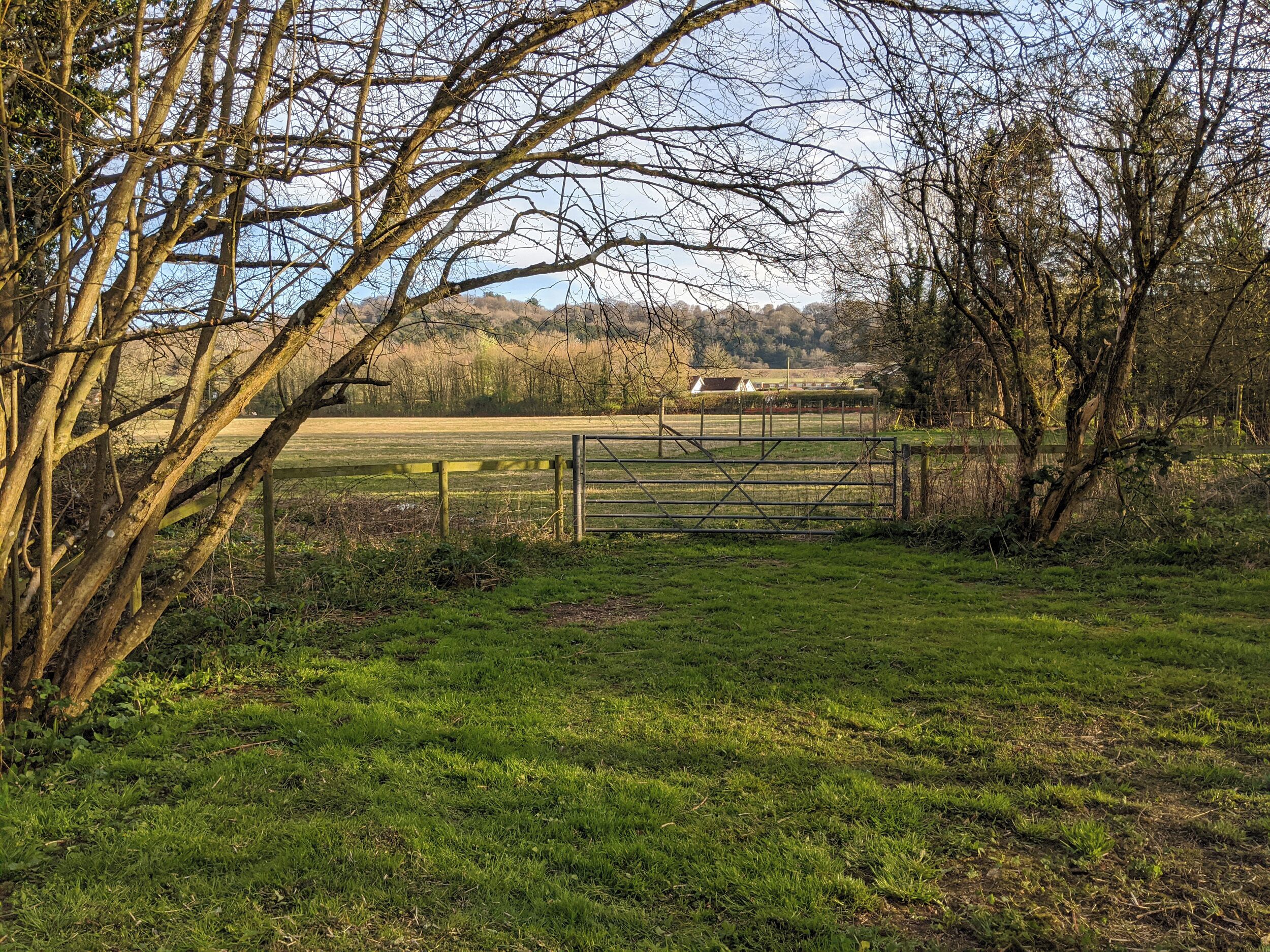 A rural landscape with a wooden gate, open fields, and a distant building.