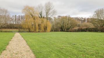 A grassy field with a gravel path leading through it, surrounded by trees and bushes.