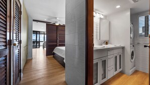 Ein modernes Hotelzimmer mit Holzboden, einem Bett, einem Badezimmer mit Waschmaschine und einem Balkon mit Blick.